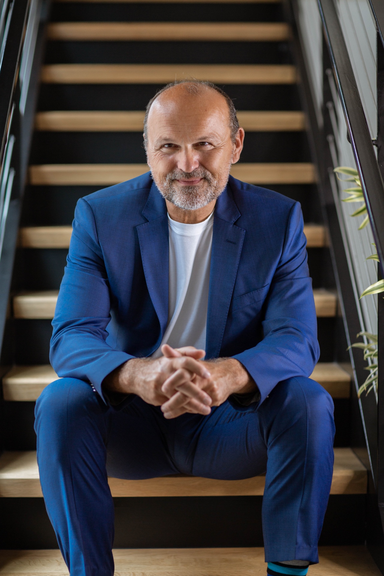 Sascha Menesi seated on a staircase, in a navy suit.